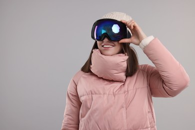 Winter sports. Happy woman with snowboard goggles on grey background, space for text