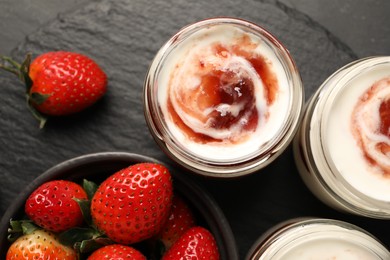 Photo of Tasty yoghurt with jam and strawberries on black table, flat lay