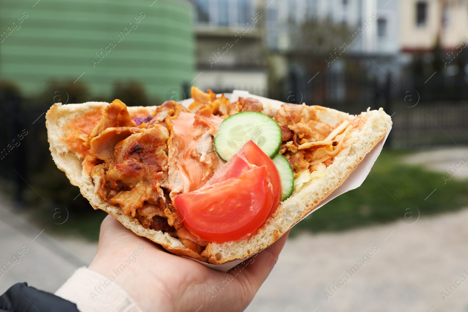 Photo of Woman holding delicious bread with roasted meat and vegetables outdoors, closeup. Street food