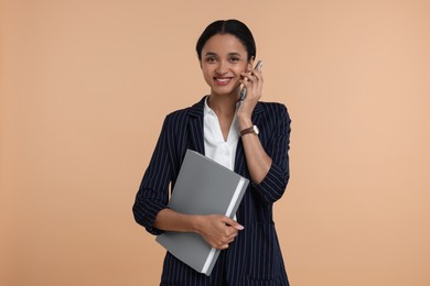 Beautiful secretary with folder talking on phone against beige background