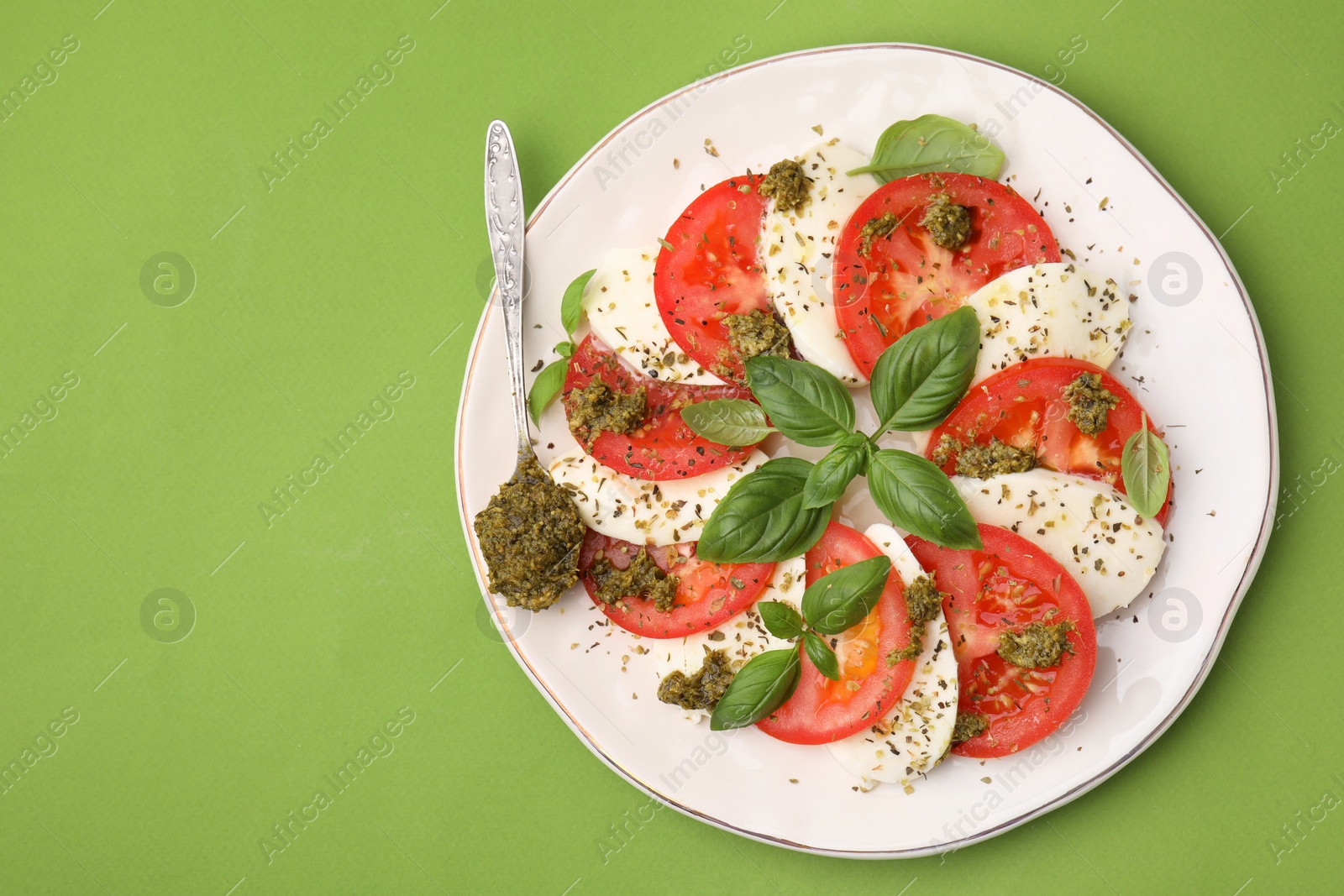 Photo of Plate of delicious Caprese salad and spoon with pesto sauce on green table, top view. Space for text