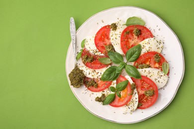 Photo of Plate of delicious Caprese salad and spoon with pesto sauce on green table, top view. Space for text