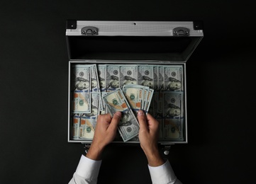 Photo of Businessman counting money over suitcase on dark background, top view