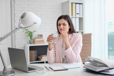Photo of Young woman taking pill against headaches while sitting at table in office