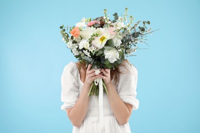 Woman covering her face with bouquet of beautiful flowers on light blue background