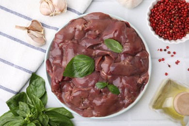 Plate of raw chicken liver with basil and products on white table, flat lay