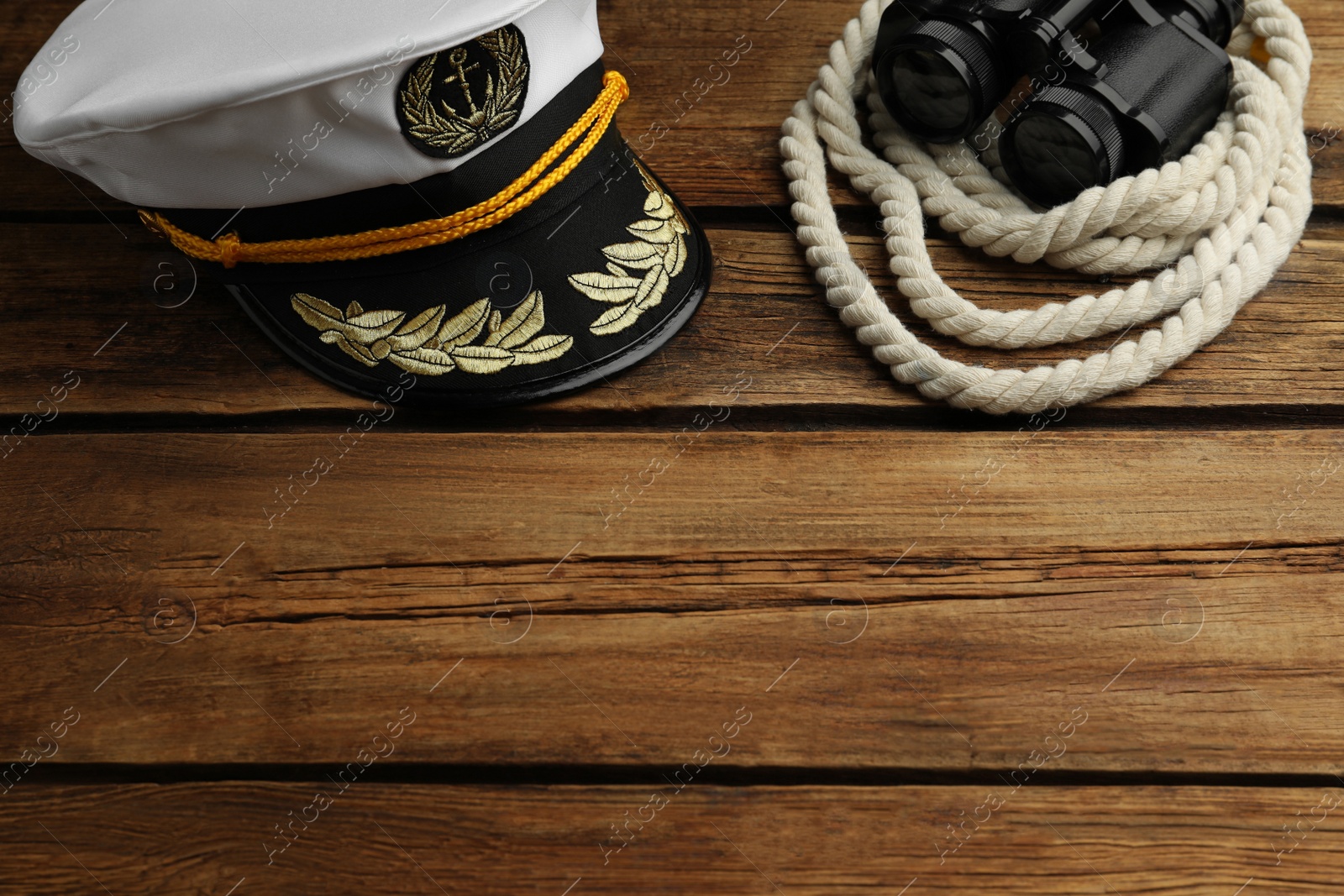 Photo of Peaked cap and rope with binoculars on wooden background, space for text