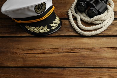 Photo of Peaked cap and rope with binoculars on wooden background, space for text