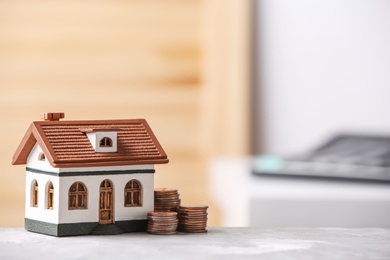 House model and coins on table against blurred background. Space for text