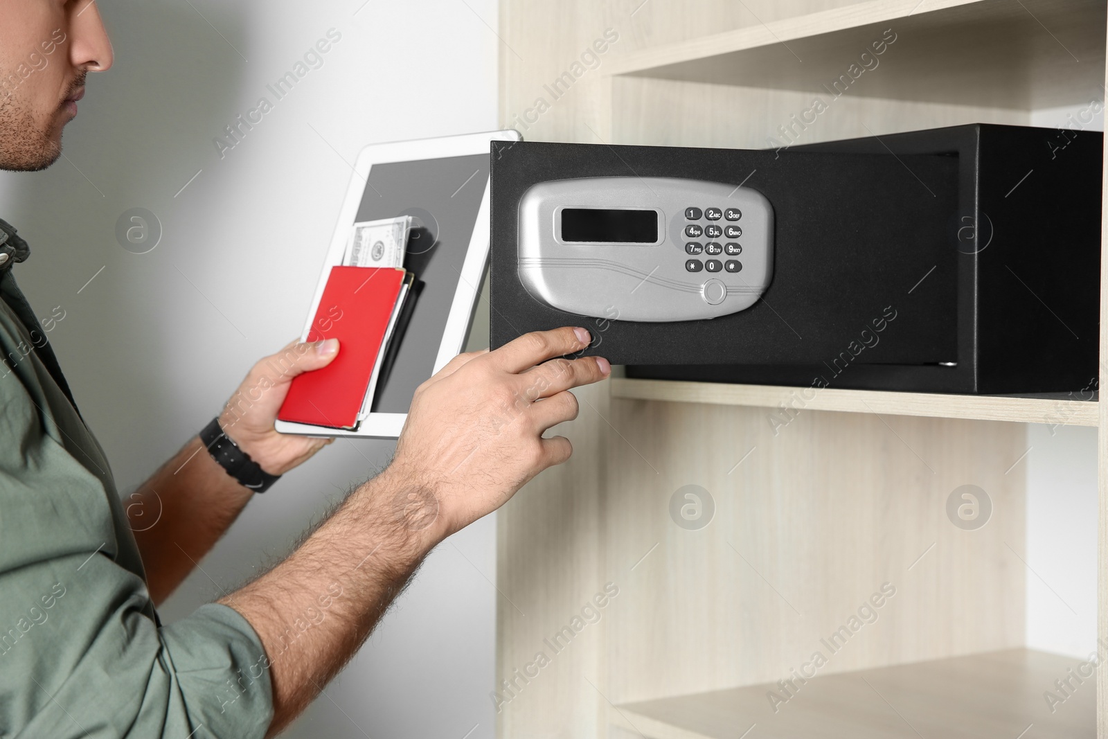 Photo of Man putting tablet, passport and money into steel safe, closeup