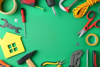 Photo of Frame of repair tools and house figure on green background, flat lay. Space for text