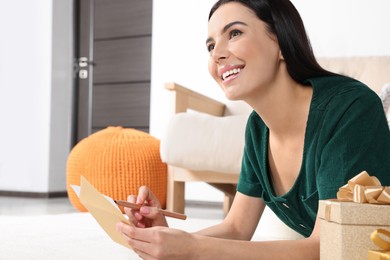 Photo of Happy woman writing message in greeting card on carpet in living room
