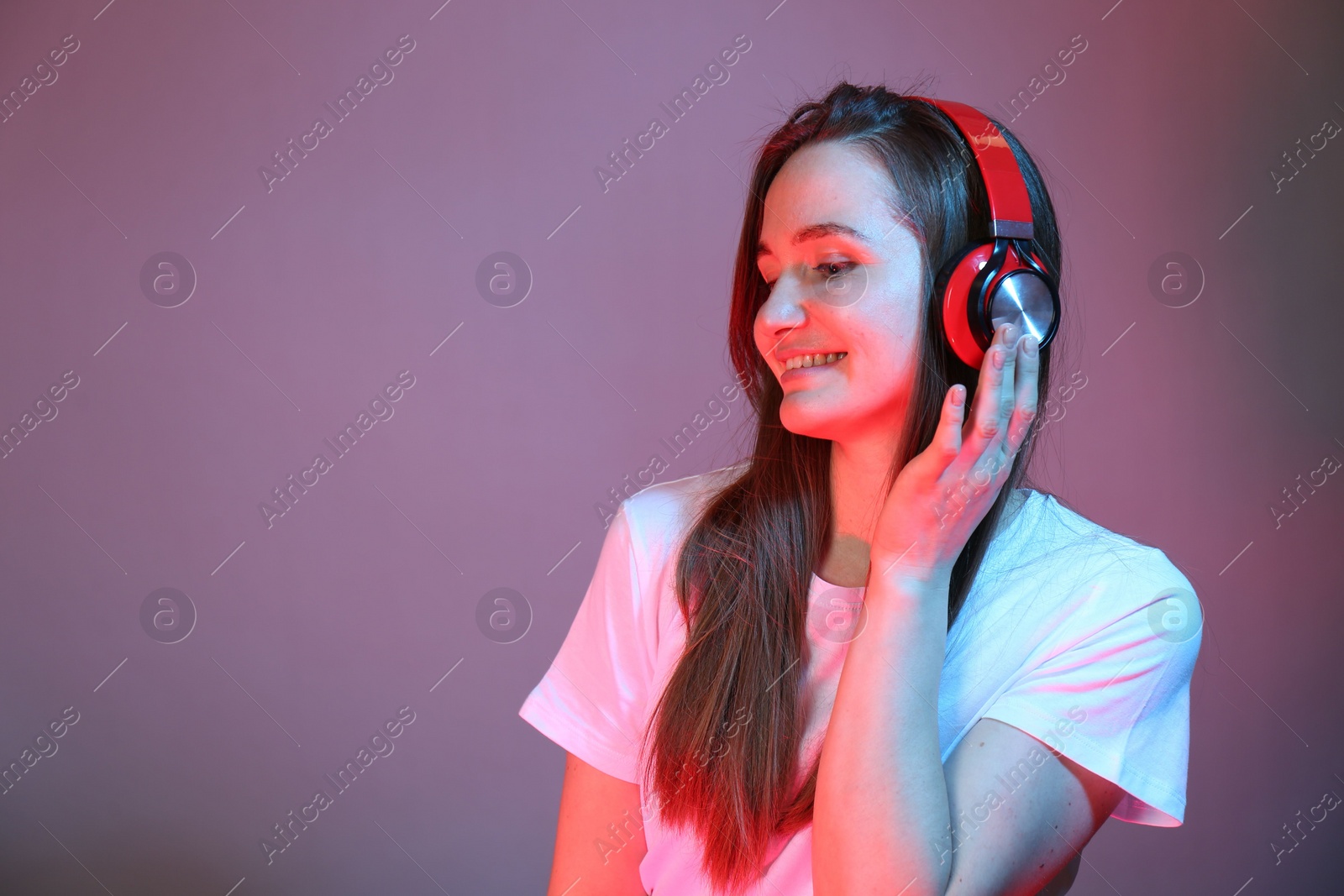 Photo of Portrait of beautiful woman with headphones in neon lights on color background, space for text