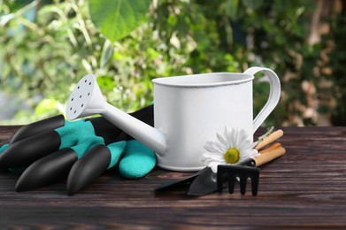 Watering can, flower and gardening tools on wooden table outdoors