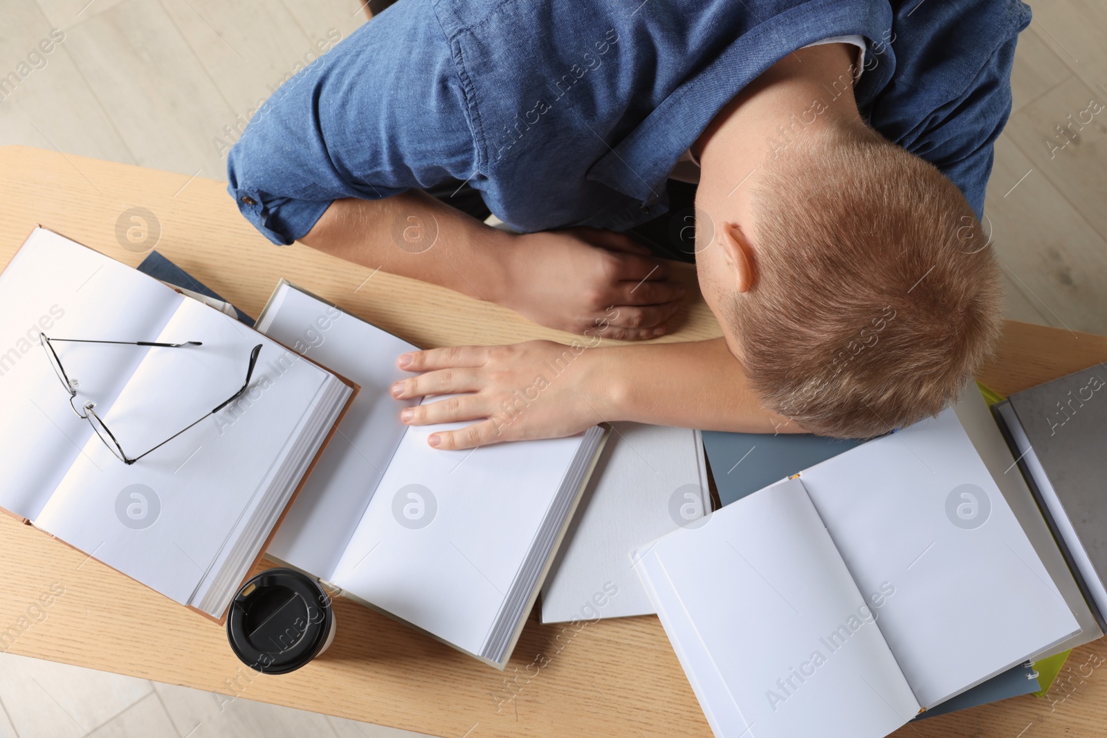 Photo of Tired man sleeping near books at wooden table, top view