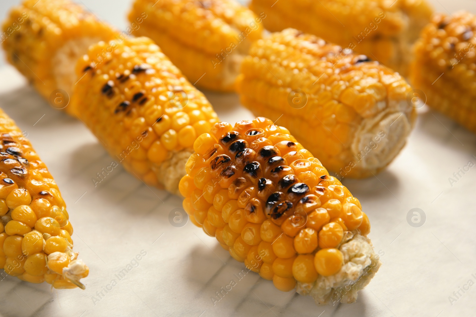 Photo of Fresh grilled tasty corn cobs on parchment paper, closeup