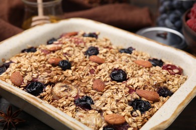 Photo of Tasty baked oatmeal with berries and almonds in baking tray on table, closeup