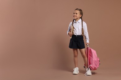 Happy schoolgirl with backpack and books on brown background, space for text