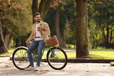 Photo of Young man with bicycle holding takeaway coffee in park, space for text