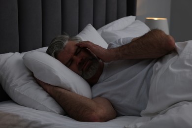 Photo of Mature man suffering from headache in bed at night