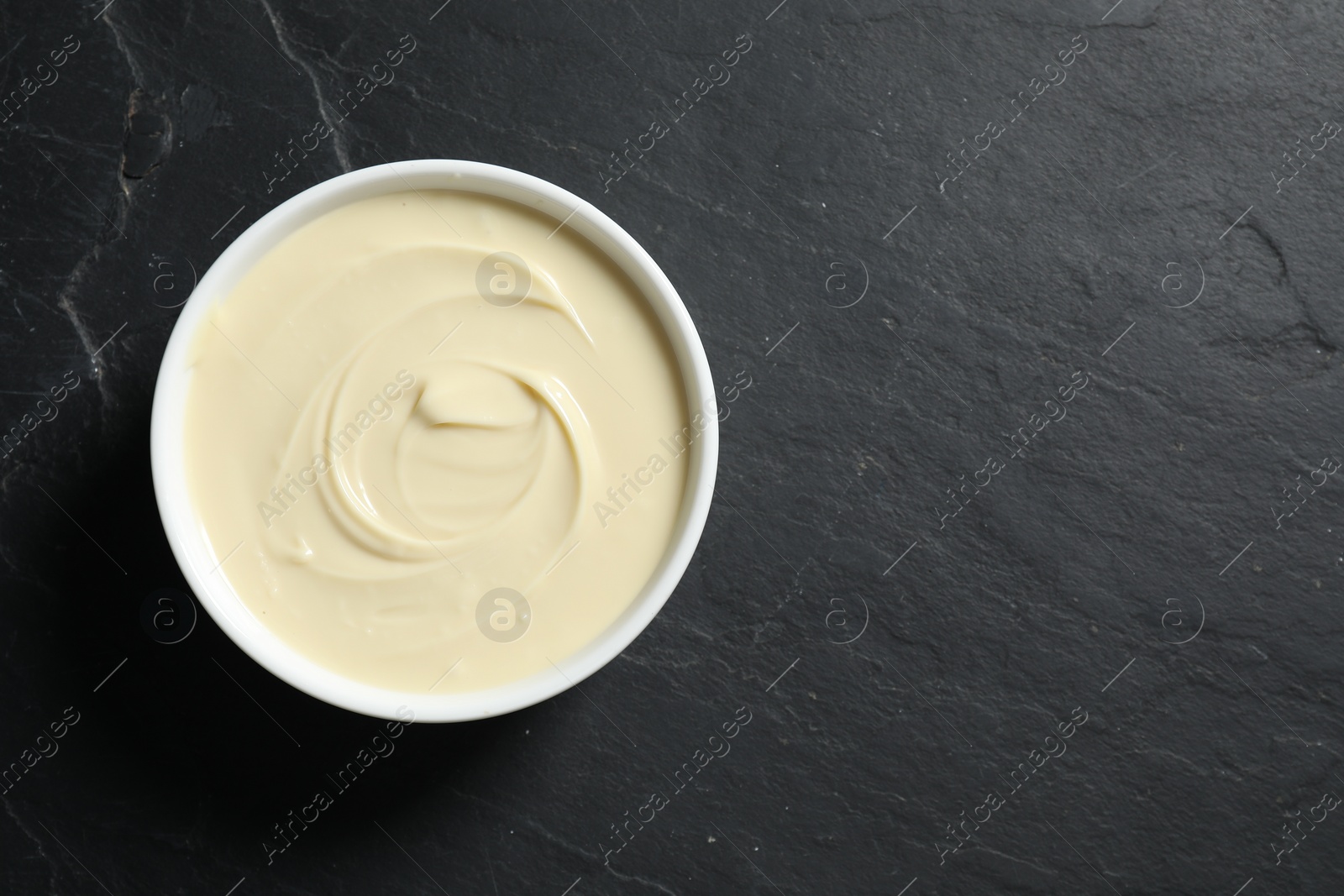 Photo of Tasty melted white chocolate in bowl on black table, top view. Space for text