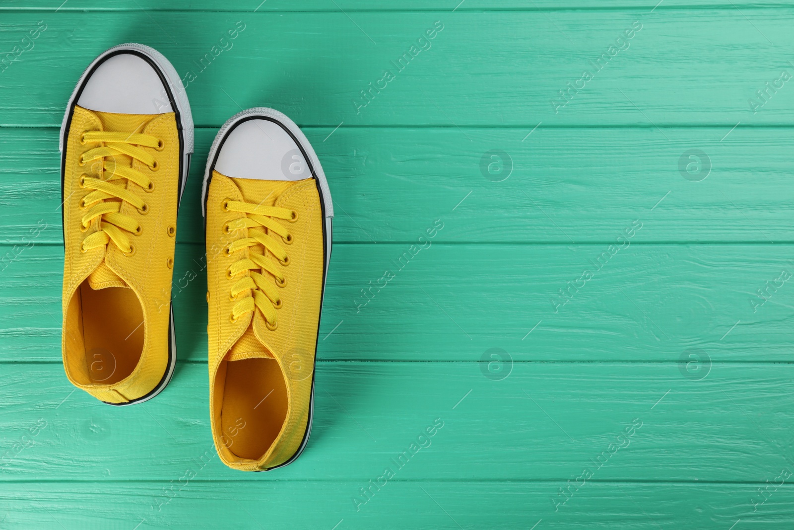 Photo of Pair of yellow sneakers on turquoise wooden table, flat lay. Space for text