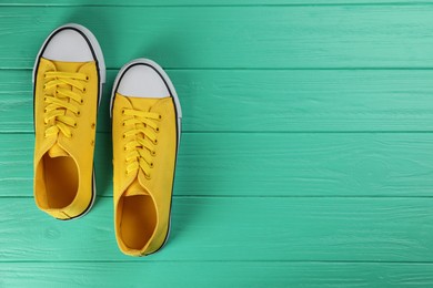 Photo of Pair of yellow sneakers on turquoise wooden table, flat lay. Space for text