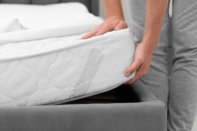 Photo of Man putting soft mattress on bed, closeup