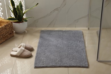 Photo of Soft grey bath mat and slippers on floor indoors