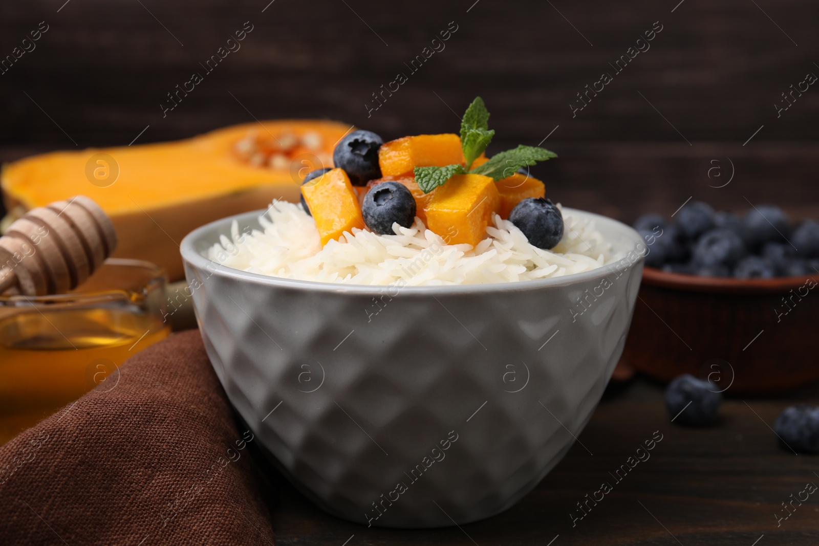 Photo of Bowl of delicious rice porridge with blueberries and pumpkin on wooden table