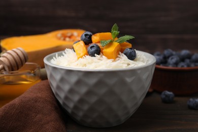 Photo of Bowl of delicious rice porridge with blueberries and pumpkin on wooden table