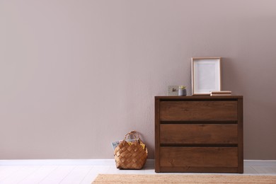 Photo of Wooden chest of drawers with decor and empty frame near light wall in room, space for text. Interior design