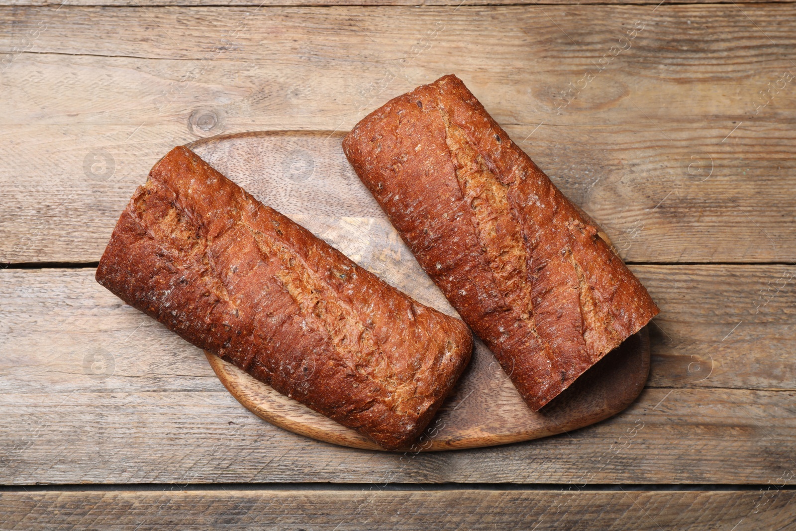 Photo of Cut rye baguette on wooden table, top view