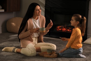 Photo of Happy mother and daughter spending time together on floor near fireplace at home