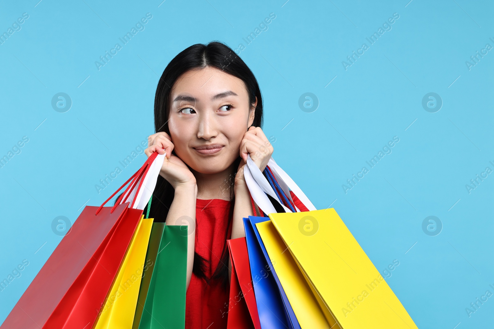 Photo of Happy woman with shopping bags on light blue background. Space for text