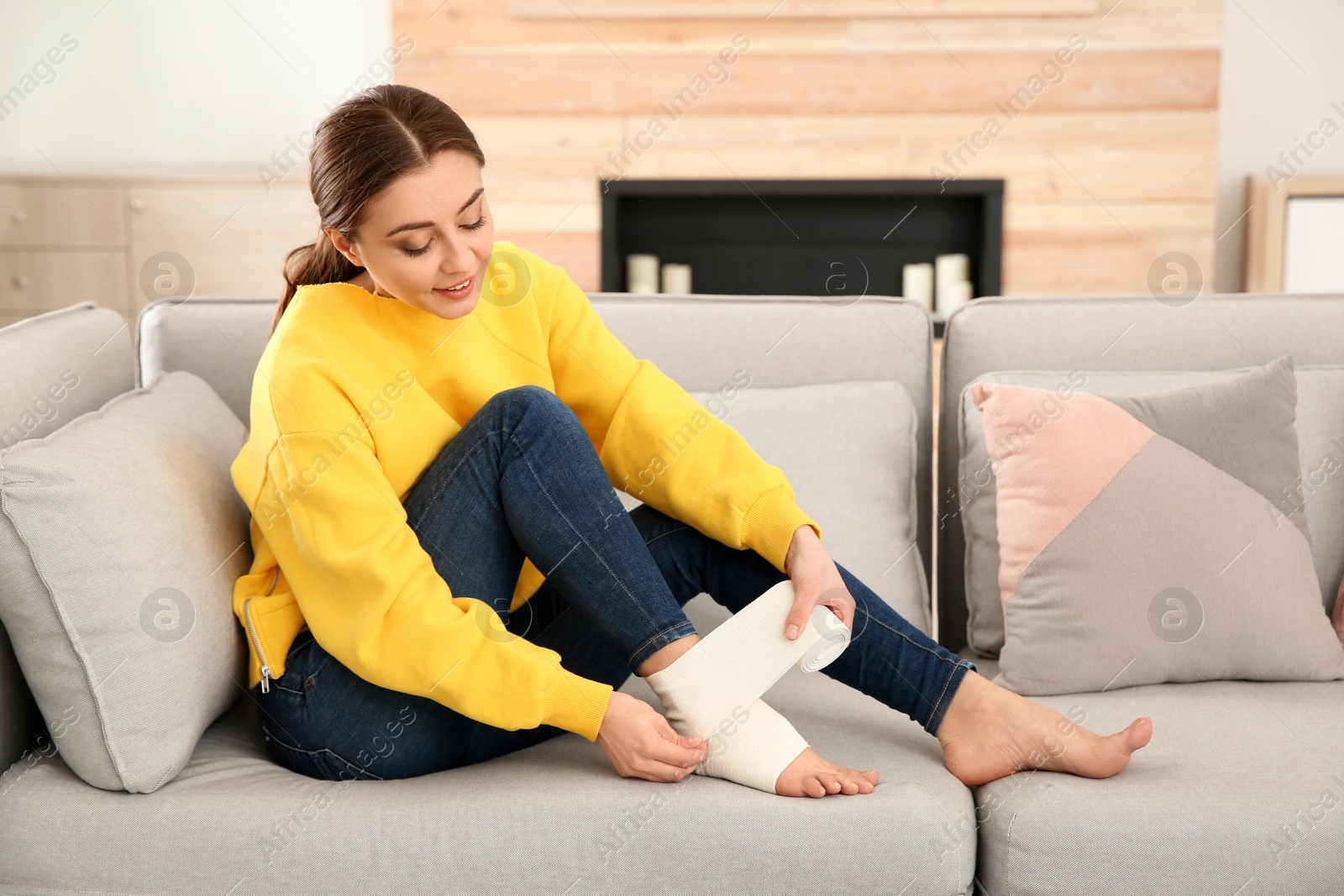 Photo of Young woman applying bandage on injured leg at home. First aid