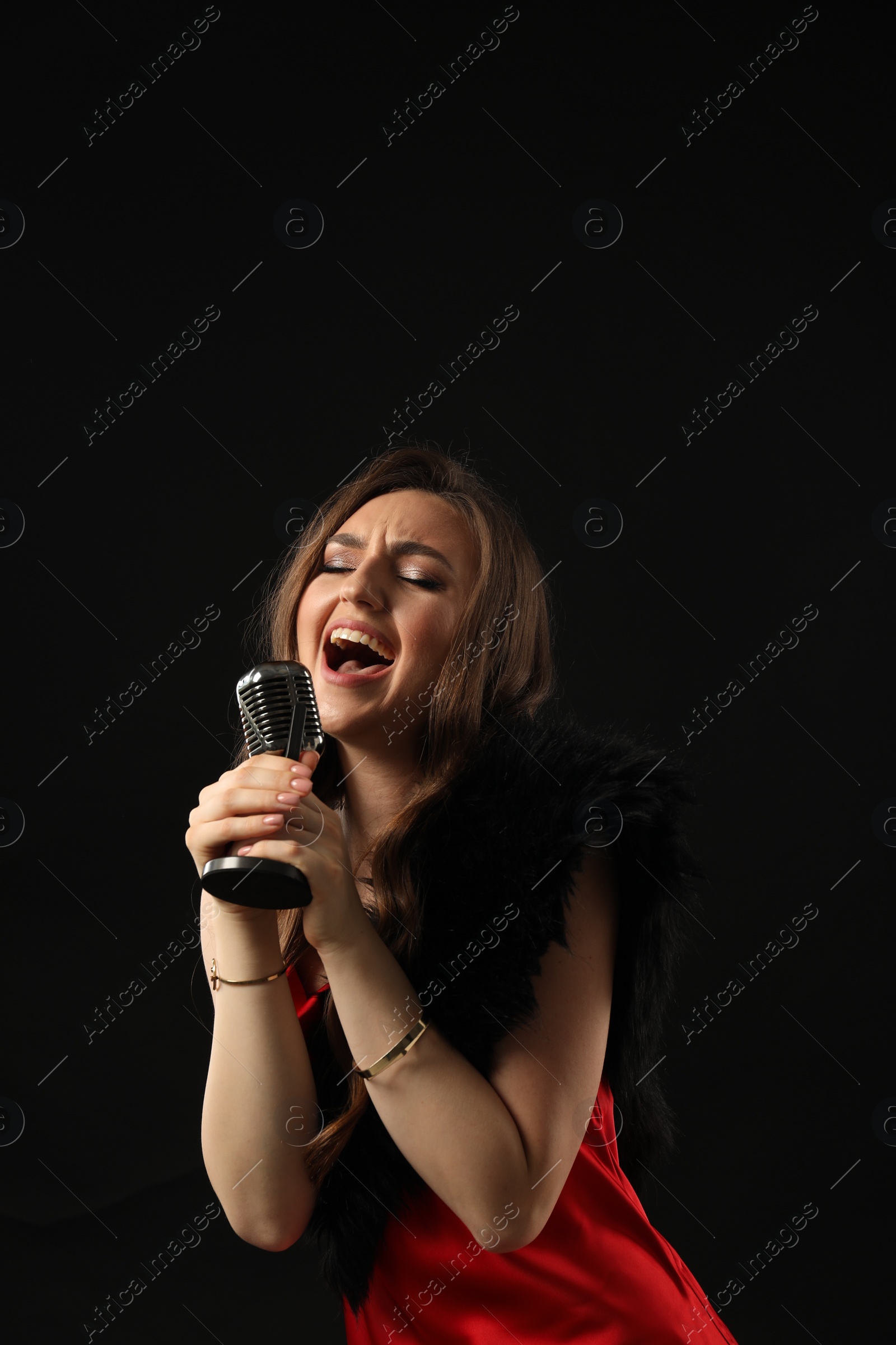 Photo of Beautiful young woman with microphone singing on black background