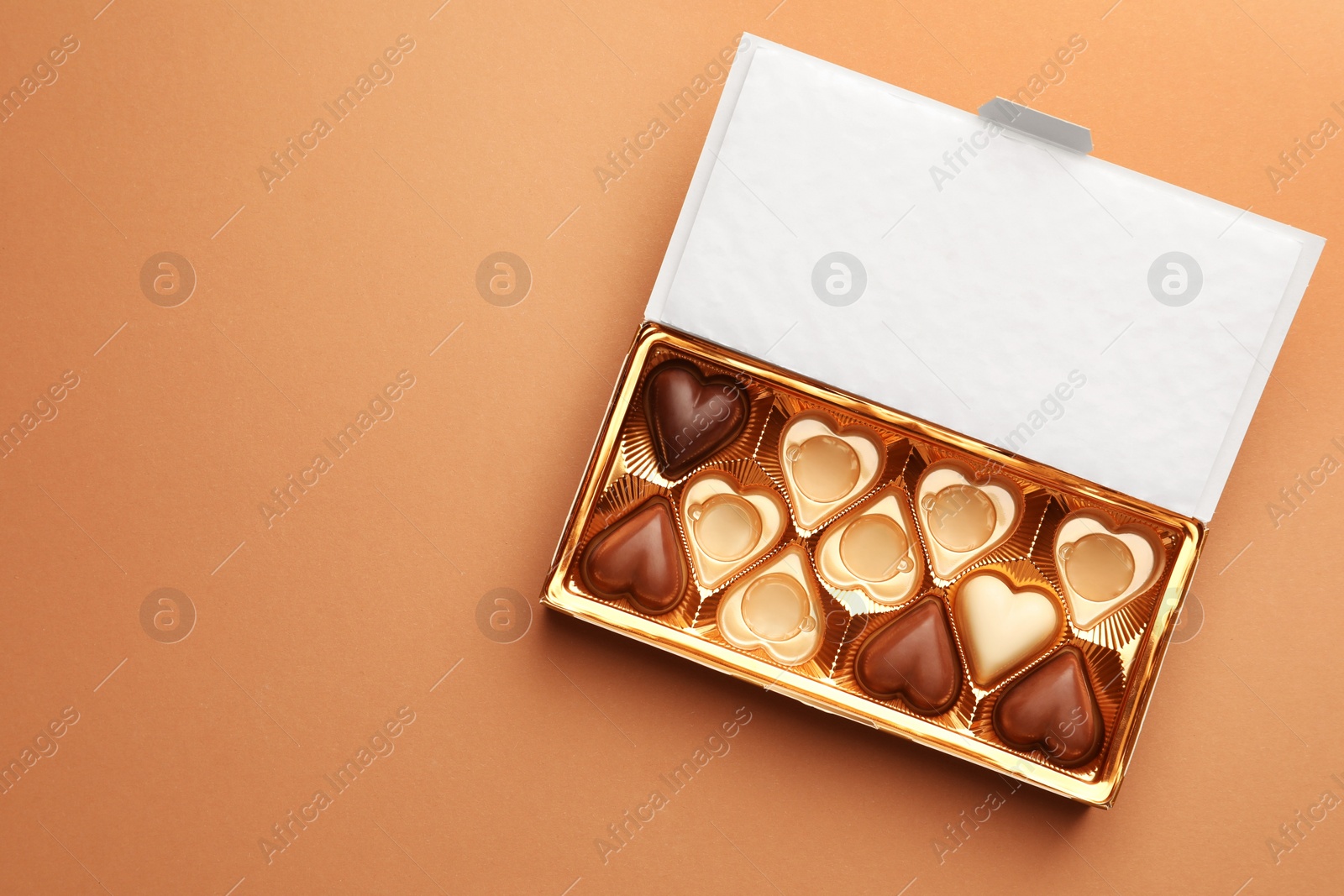 Photo of Partially empty box of chocolate candies on light brown background, top view. Space for text