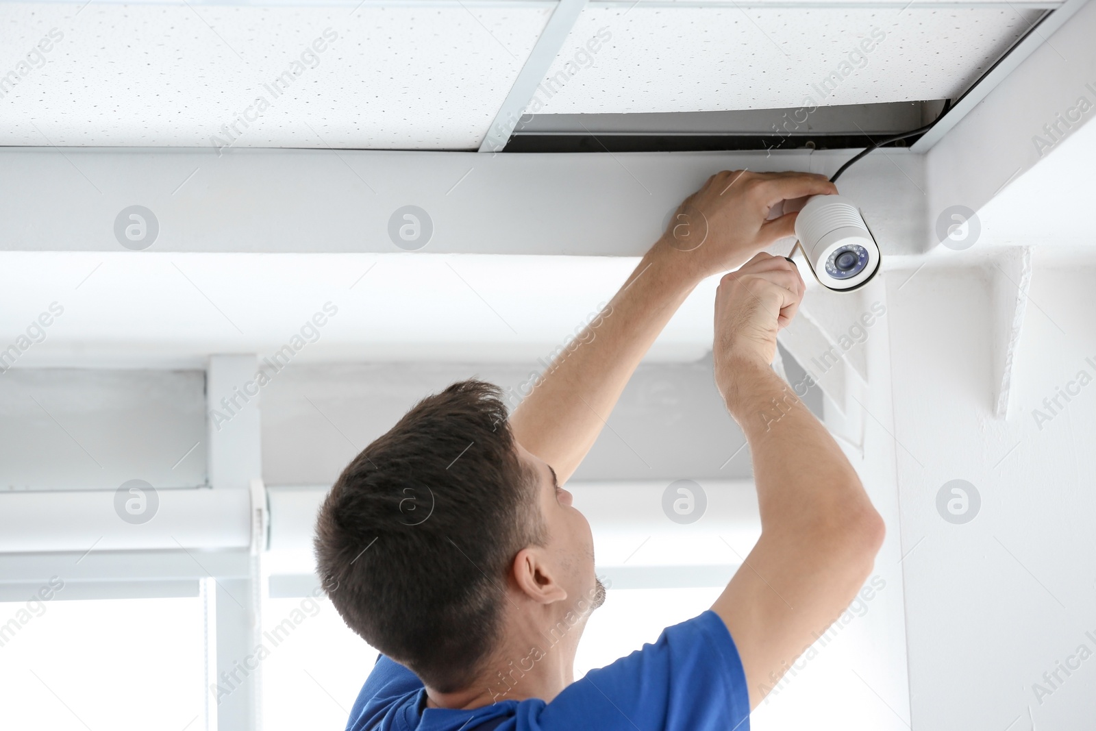 Photo of Technician installing CCTV camera on ceiling indoors