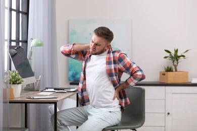 Photo of Young man suffering from back pain in office