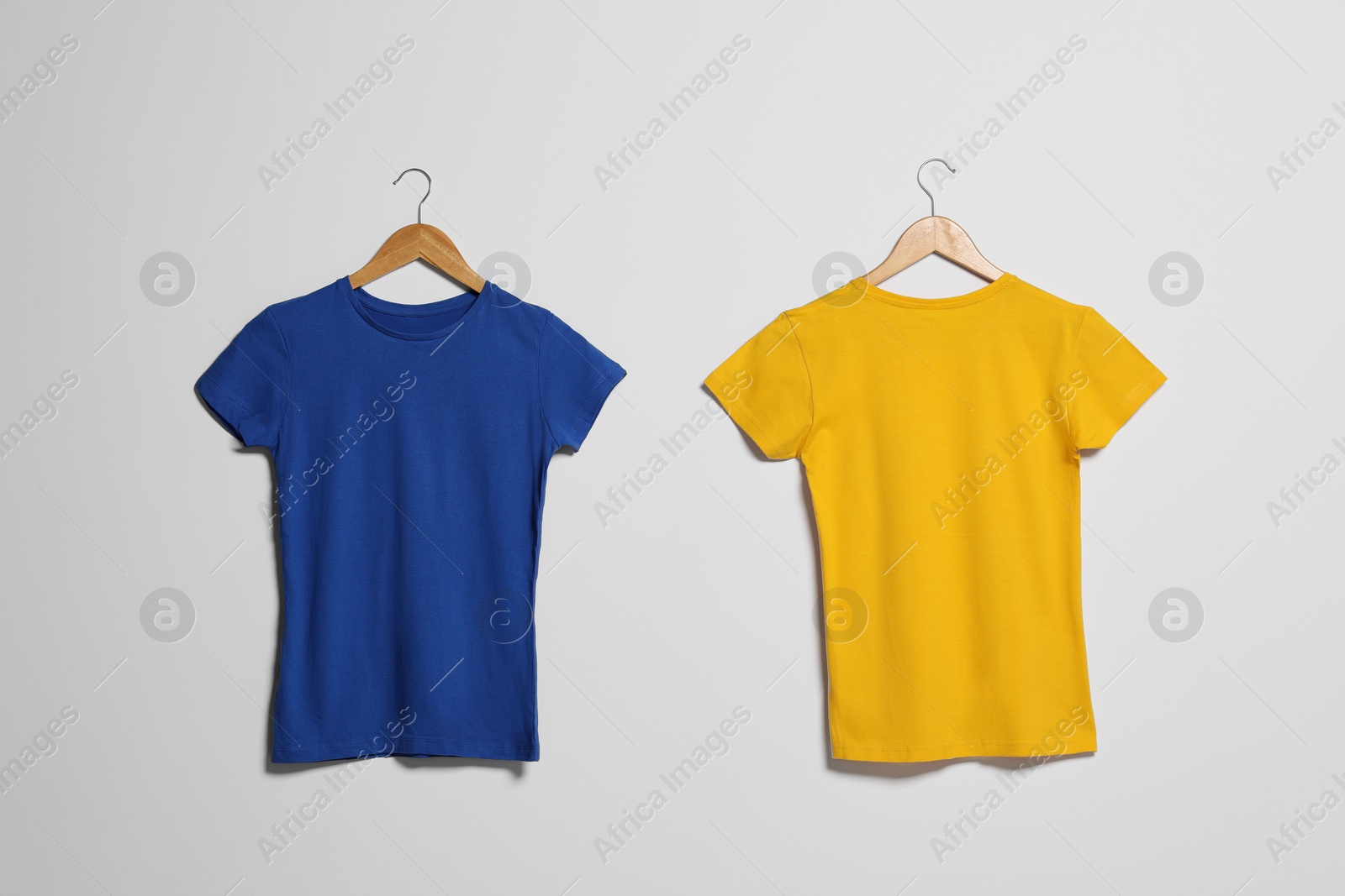 Photo of Hangers with different t-shirts on light wall. Mockup for design