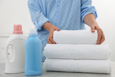 Photo of Woman folding clean towel near bottles of laundry detergents at table, closeup