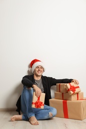 Photo of Young man with Christmas gifts near white wall