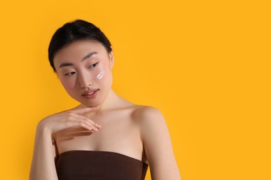 Photo of Beautiful young woman with sun protection cream on her face against orange background, space for text