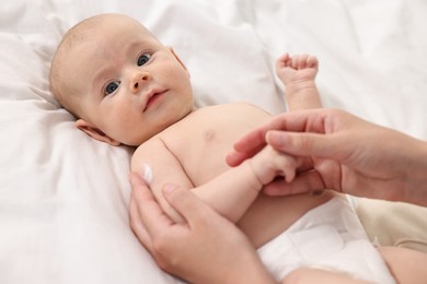 Woman applying body cream onto baby`s skin on bed, closeup