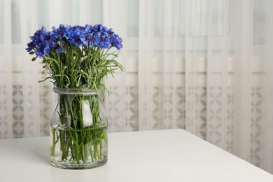 Bouquet of beautiful cornflowers in glass vase on light table at home. Space for text
