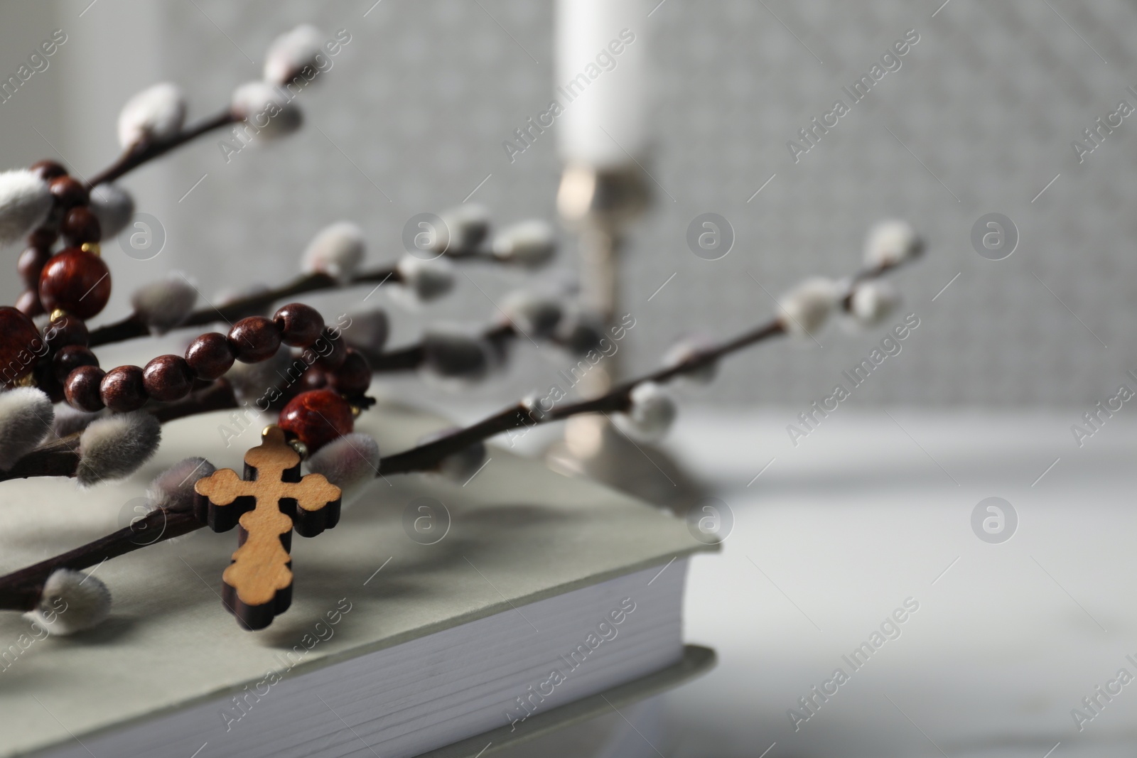 Photo of Rosary beads, book and willow branches on light table, closeup. Space for text