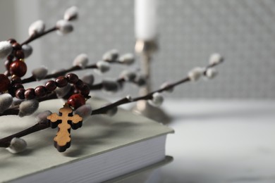 Rosary beads, book and willow branches on light table, closeup. Space for text