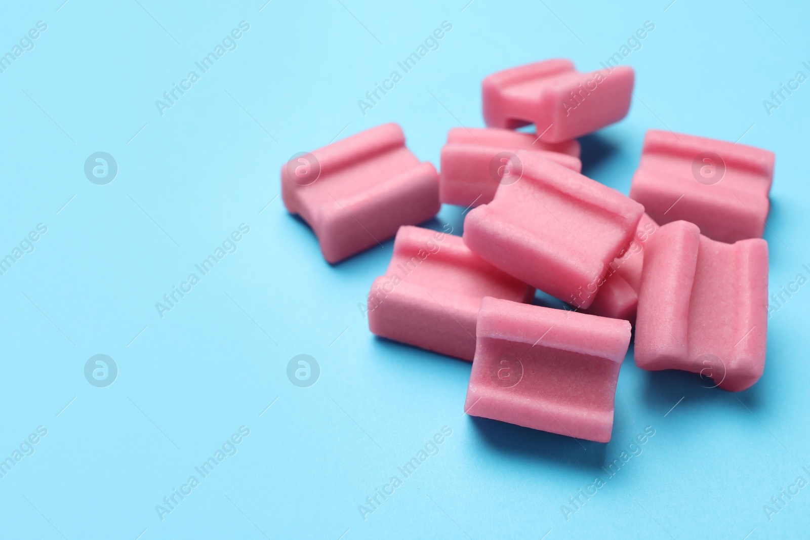 Photo of Tasty pink chewing gums on light blue background, closeup. Space for text