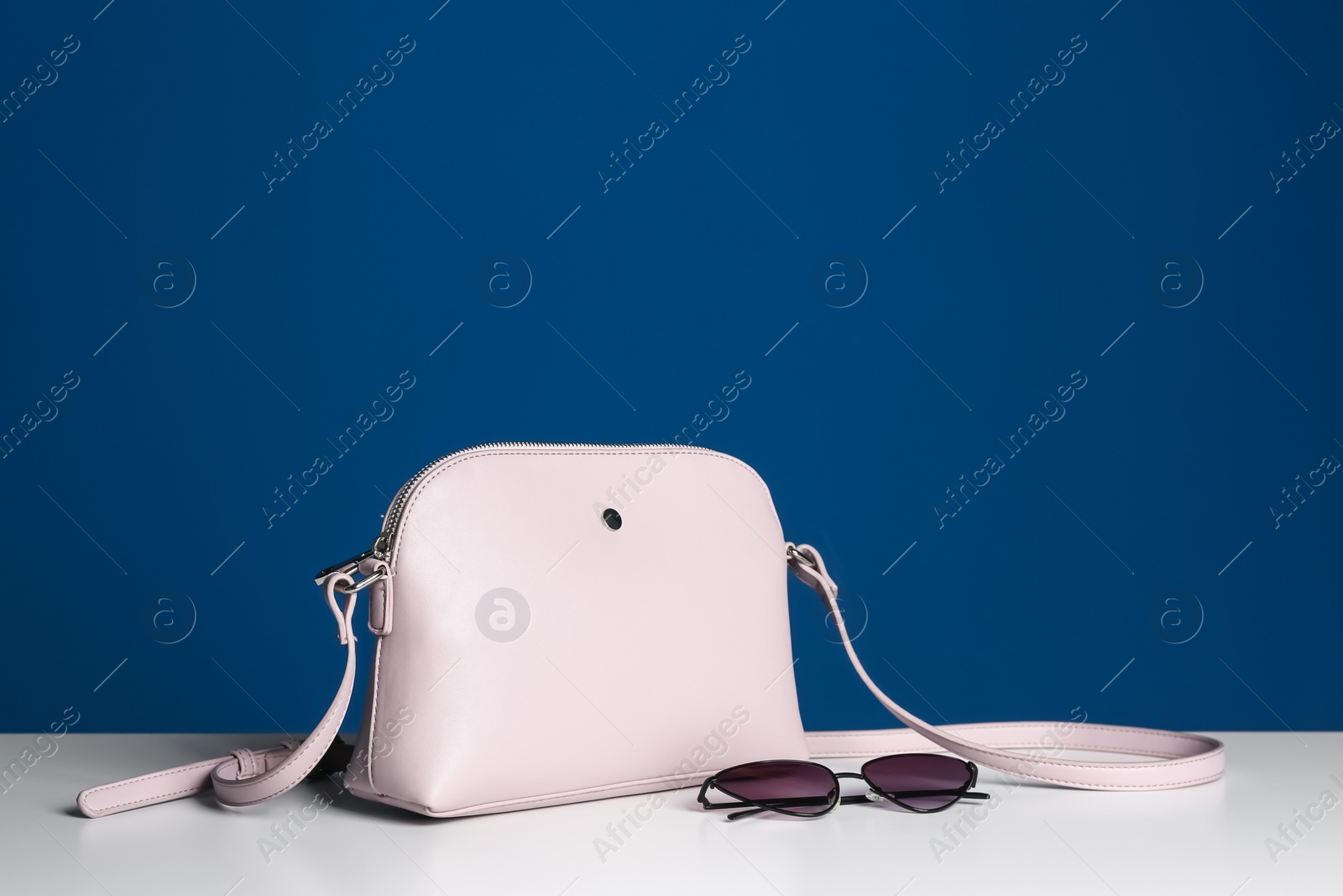 Photo of Stylish woman's bag and sunglasses on white table. Space for text
